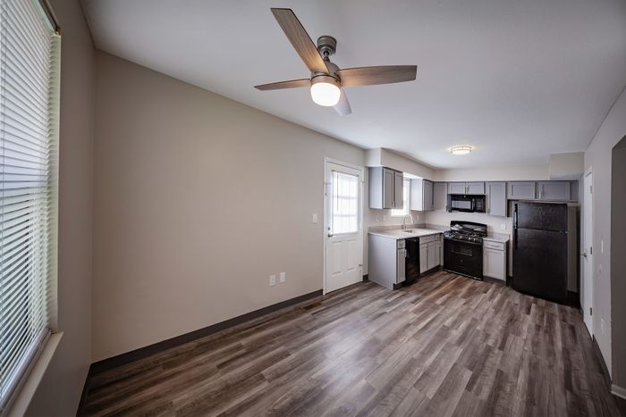 Chic open-concept kitchen with modern grey cabinets, sleek appliances, and warm wood floors, enhanced by natural light and a contemporary ceiling fan.