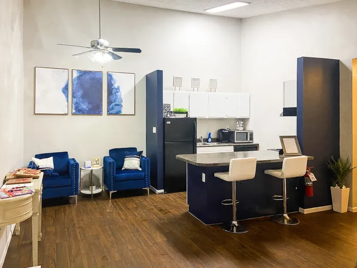 Chic open-concept living room and kitchen with modern art, elegant blue chairs, and sleek breakfast bar seating.