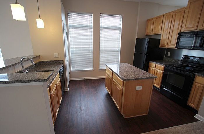 Modern kitchen with elegant granite countertops, sleek black appliances, and natural wood cabinetry, offering a bright and inviting cooking space.