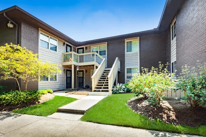 Charming two-story apartment entrance surrounded by lush green landscaping.