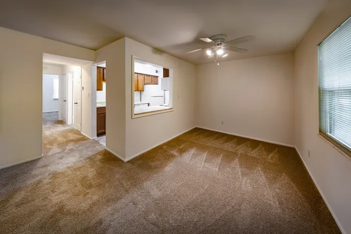Inviting living room with plush carpeting, ceiling fan that connects into a cozy kitchen with wood cabinetry.