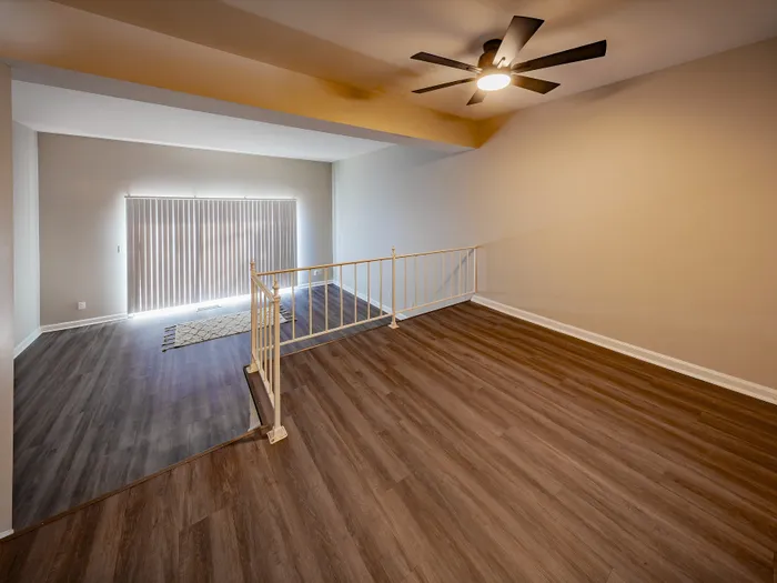 Inviting open-plan living area with elegant wood flooring and natural light from expansive windows, featuring a modern ceiling fan.