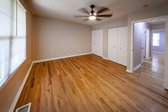 Bright, inviting room with elegant hardwood floors, ceiling fan, large windows, and ample closet space.