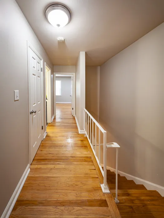 Bright hallway with elegant wooden flooring leading to spacious rooms, featuring a modern staircase and updated fixtures.
