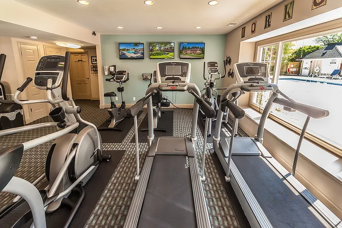 Modern fitness center with state-of-the-art treadmills and elliptical machines, and large windows offering a pool view.
