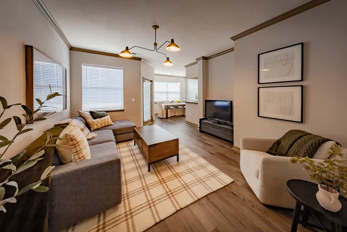 Inviting living room with modern decor, cozy gray sectional, and elegant lighting, featuring a sleek TV setup and charming dining nook in view.