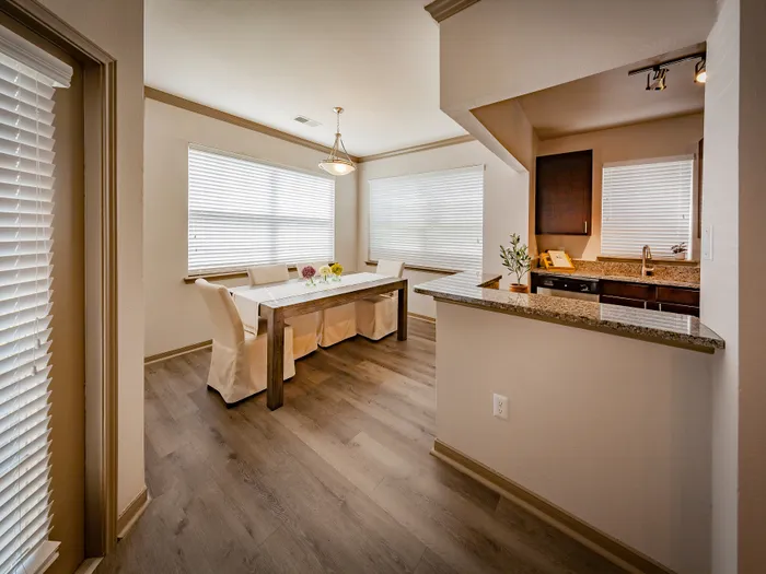 Bright dining area with sleek hardwood floors adjacent to a modern kitchen featuring granite countertops and elegant lighting.