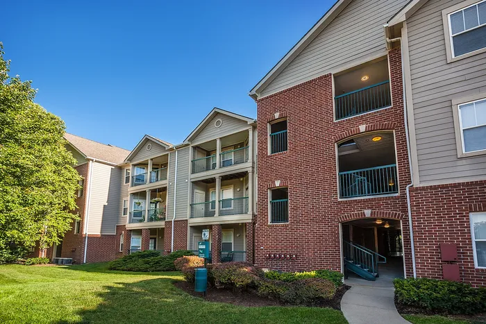 Charming brick and siding apartment building with spacious balconies, nestled in a lush green setting under a clear blue sky.