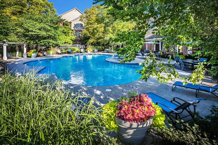 Inviting poolside oasis with lush greenery, vibrant flowers, and comfortable lounge chairs in a serene apartment complex setting.