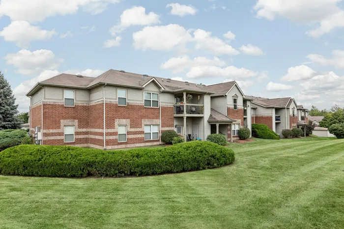 Charming brick apartment complex with lush greenery and spacious balconies, set under a picturesque blue sky.