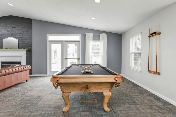 Inviting recreational lounge with a stylish pool table and cozy leather sofa by a modern fireplace.