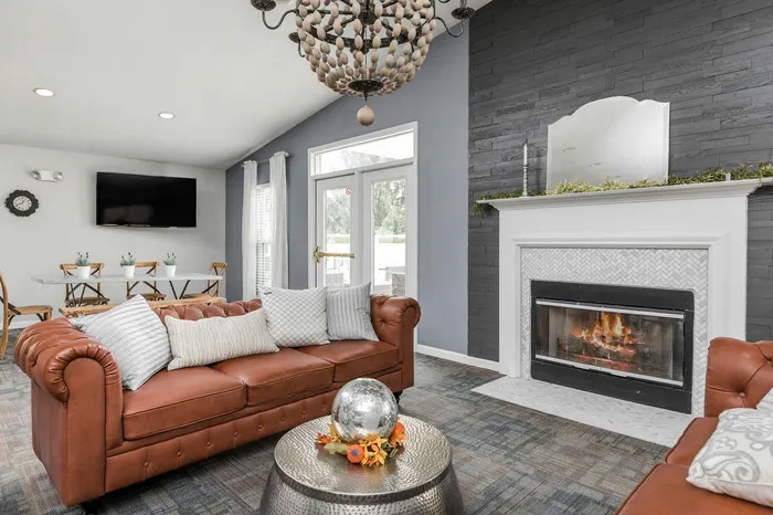 Sophisticated living room with a plush leather sofa, warm fireplace, and modern chandelier, perfect for relaxation and entertaining.
