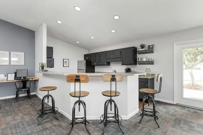 Modern kitchen with sleek black cabinets, a stylish breakfast bar with wooden stools, and a cozy workspace in the corner.