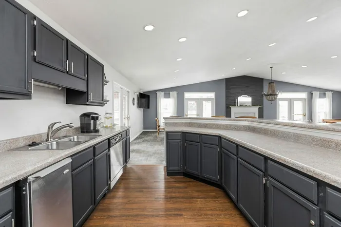 Modern kitchen with sleek dark cabinetry, stainless steel appliances, and an open concept leading to a stylish living area with ample natural light and elegant chandelier.