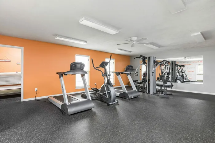 Modern apartment gym with bright orange accent wall, featuring treadmills, elliptical, and multi-station workout equipment.
