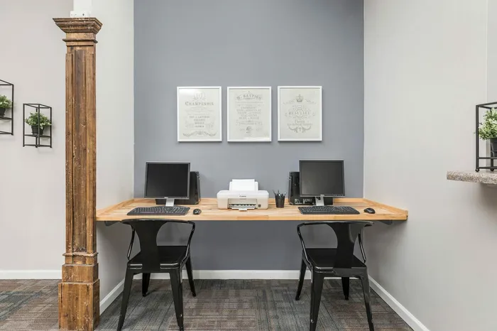 Contemporary home office setup with dual computer stations, elegant wooden accents, and stylish framed art pieces on a calming gray wall.