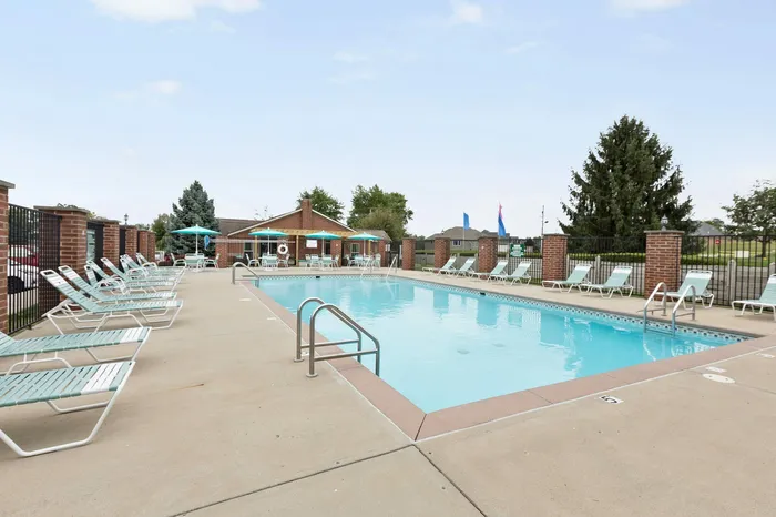 Inviting outdoor swimming pool with modern lounge chairs and vibrant umbrellas, offering a perfect relaxation spot in a serene community setting.