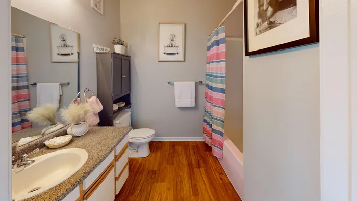Charming bathroom with elegant granite countertops, warm wood flooring, and vibrant striped shower curtain.