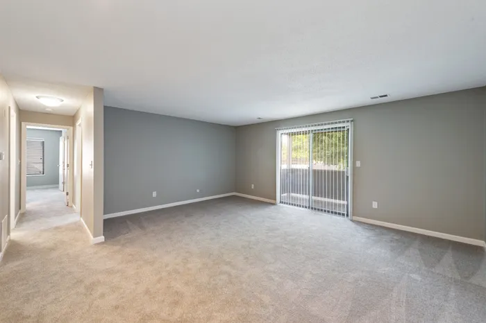 Spacious living room with plush carpeting and natural light streaming through large sliding glass doors.