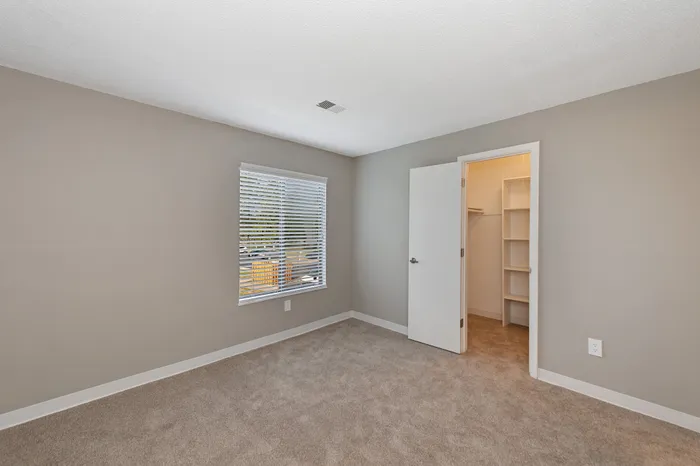 Bright and spacious bedroom with plush carpet, large window, and a walk-in closet with ample shelving, perfect for comfortable living.