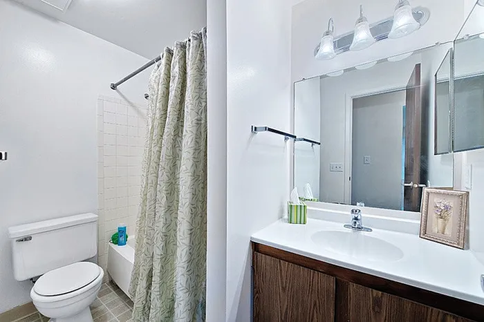 Elegant modern bathroom featuring a sleek wooden vanity, polished mirror with stylish lighting, and a pristine white bathtub.