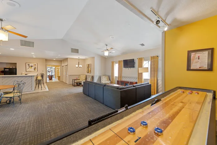 Inviting clubhouse space featuring a cozy seating area, modern bar counter, and a fun shuffleboard table.