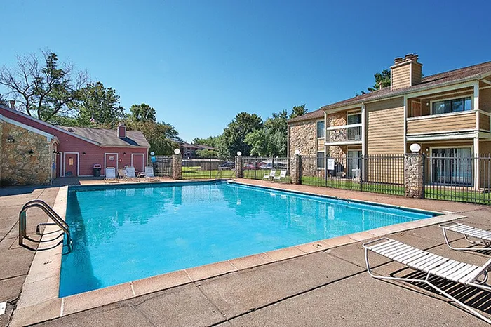Inviting apartment community with a sparkling blue pool surrounded by sun loungers and lush greenery, offering a perfect retreat for relaxation and leisure.