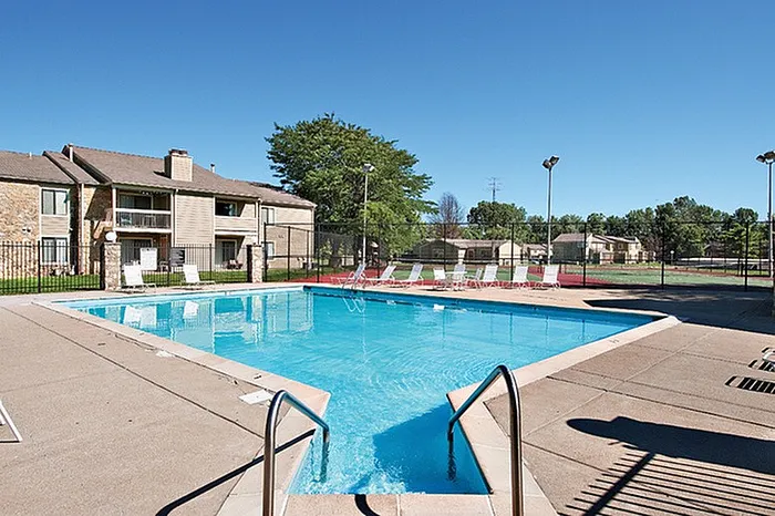 Inviting outdoor pool area in a residential complex with sun loungers and lush greenery, offering a perfect relaxation spot.