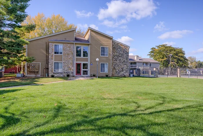 Charming stone-accented apartment building with lush green lawn, ideal for relaxed suburban living.