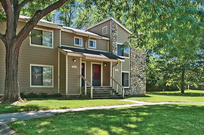 Charming two-story apartment with elegant stone facade, surrounded by lush greenery and bathed in natural light.