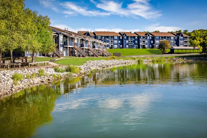 Charming lakeside apartments with blue exterior, nestled in scenic greenery, offering a tranquil living environment.