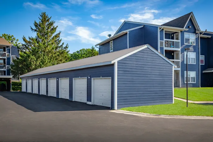 Charming apartment exterior with blue siding, private balconies, and modern garage units, set against a vibrant green landscape.
