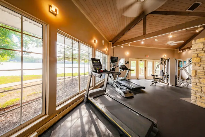 Bright and airy fitness center with modern treadmills and strength-training equipment, featuring expansive windows showcasing a serene lakeside view.