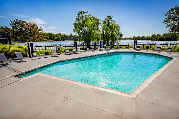 Inviting outdoor pool area with lounge chairs and lush greenery, overlooking a serene lakeside view under a clear blue sky.