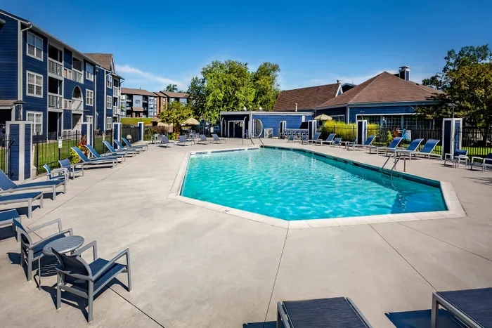 Inviting apartment complex with a pristine outdoor pool, surrounded by comfortable lounging chairs under clear blue skies.
