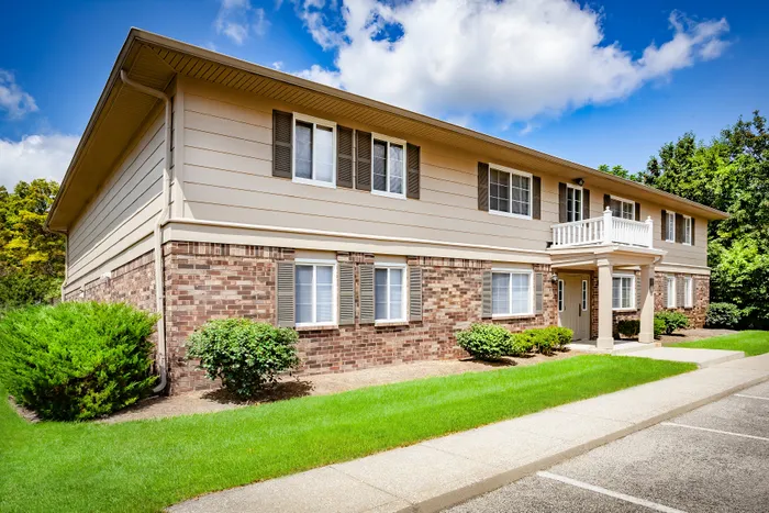 Charming two-story brick apartment building with elegant white trim, nestled in well-manicured greenery under a vibrant blue sky.
