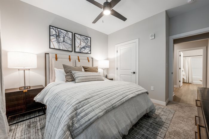 Inviting bedroom with elegant contemporary decor, featuring a plush bed, stylish nightstands, modern ceiling fan, and artful wall paintings.