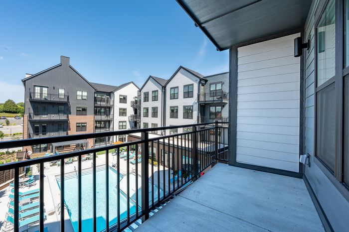 Modern apartment balcony view overlooking a pristine swimming pool and stylish residential buildings under clear blue skies.
