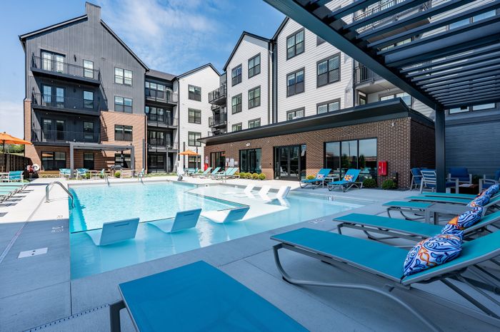 Chic modern apartment building with a beautiful sunlit pool area, featuring stylish lounge chairs and vibrant decor.