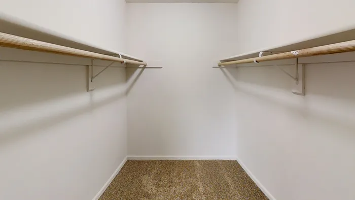 Spacious walk-in closet with dual wooden hanger rods, featuring neutral carpeting and bright white walls.
