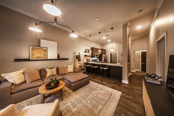 Elegant living space with cozy sectional sofa, chic lighting, and open kitchen with bar seating, exuding modern comfort and style.