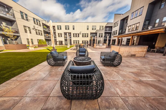 Modern apartment courtyard featuring stylish outdoor seating, vibrant green lawn, and sleek architecture under a clear blue sky.