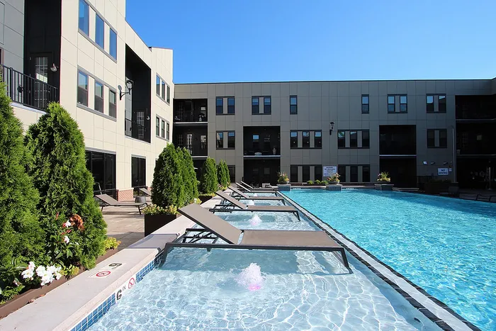 Luxurious apartment complex featuring a pristine outdoor pool, stylish lounge chairs, and lush greenery, perfect for relaxation and leisure.