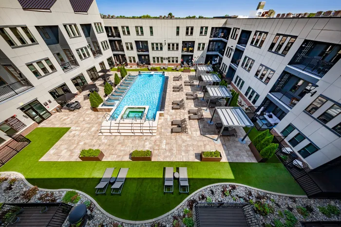 Luxurious apartment community courtyard featuring a sparkling swimming pool, relaxing lounge chairs, and modern pergolas set against lush greenery.