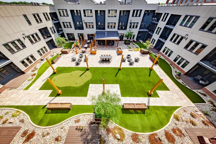 Modern apartment community courtyard featuring lush green lawn, cozy seating areas, and a stylish putting green, perfect for relaxation and leisure.