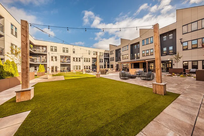 Modern apartment courtyard featuring lush green lawns, cozy seating areas, and stylish architecture under a clear blue sky.
