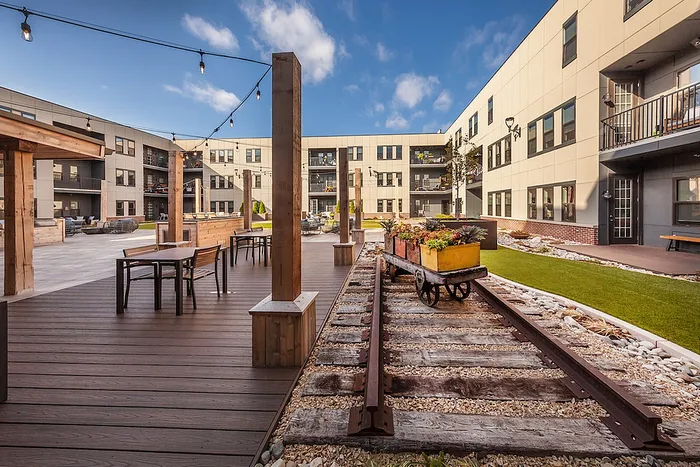 Charming apartment courtyard with rustic railway accents, lush greenery, and inviting outdoor seating areas.