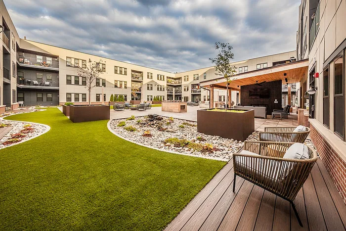 Modern apartment courtyard with lush green lawn, stylish outdoor seating, and elegant landscaping.