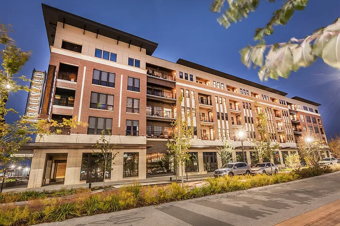 Chic urban apartment building with a modern brick facade, illuminated at dusk, offering stylish balconies and vibrant city-life ambiance.