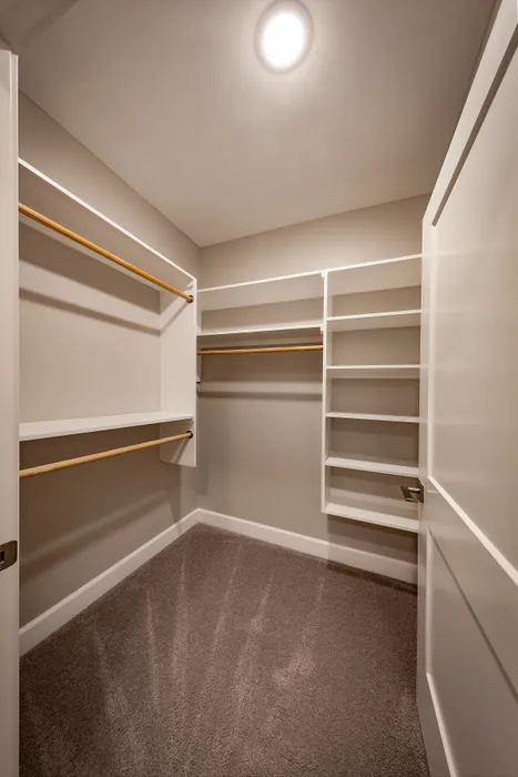 Spacious walk-in closet featuring elegant white shelving and ample hanging space, illuminated by soft lighting for a luxurious experience.